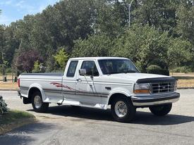 A 1995 Ford F-250 pickup truck with a white exterior and red stripe detail parked on a street