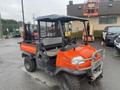 A 2010 Kubota RTV 900 side-by-side utility vehicle with an orange body and a black canopy, featuring a front bumper and a flatbed cargo area