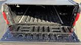 A 2016 Ford F-150 truck bed with a black plastic liner showing some dirt and debris inside