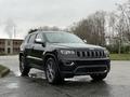 A black 2019 Jeep Grand Cherokee with a sleek design and silver accents parked on a wet surface with trees in the background
