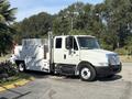 A white 2006 International 4300 truck with a service body and equipment compartments on the side