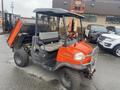 A 2010 Kubota RTV 900 utility vehicle with a distinctive orange and black design has a cargo bed raised at the rear and features a seat for the driver in the front