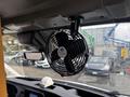 A black portable fan mounted on the dashboard of a vehicle