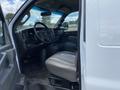 Interior view of a 2023 GMC Savana with a beige leather driver's seat and a black dashboard featuring controls and a gear shift. The steering wheel is visible in the foreground