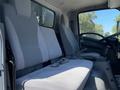 Interior view of a 2016 Isuzu NPR-HD showing two gray upholstered seats in the cab with seat belts and a steering wheel visible