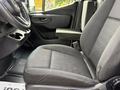 A 2023 Mercedes-Benz Sprinter with a driver's seat featuring a black fabric design and a simple dashboard including cup holders and controls