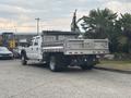 A white 2014 Ford F-550 truck with a flatbed and silver metal side panels parked on a concrete surface