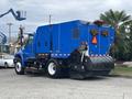 A blue 2013 International DuraStar 4300 street sweeper with front and rear brushes and warning lights