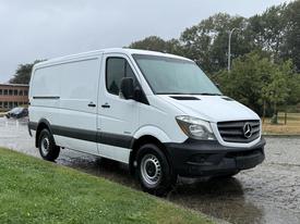 A white 2016 Mercedes-Benz Sprinter van with a high roof and sliding side door parked on a wet surface