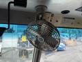 A metal desk fan mounted on a vehicle interior provides airflow to the cabin