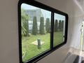 A large window with a black frame showing green shrubbery and a grassy area outside the Shuttle Office