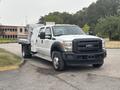 A 2014 Ford F-550 with a white exterior featuring a flatbed and tool storage compartments on the side facing slightly to the right