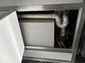 A white rectangular tank connected to various pipes inside a compartment of a 2020 Freightliner MT45
