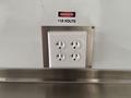 A white electrical outlet with four sockets labeled 115 volts next to a red and black danger sign
