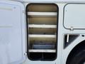 An open compartment of a 2013 International 7400 showing white shelves and a sliding tray for storage