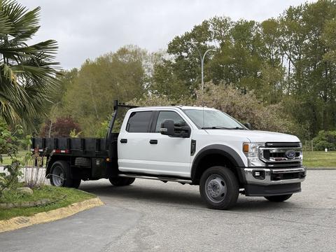 A 2020 Ford F-550 truck with a flatbed and dual rear wheels in a light color positioned at an angle showing its front and side