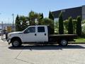 A white 2012 Ford F-350 SD flatbed truck with a double cab parked with wooden planks on the flatbed and chrome wheels