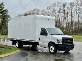 A 2024 Ford E-450 box truck with a white cargo area and a cab painted in silver, parked at an angle with its wheels on the pavement