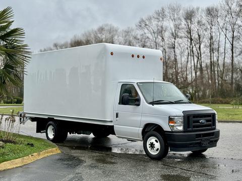 A 2024 Ford E-450 box truck with a white cargo area and a cab painted in silver, parked at an angle with its wheels on the pavement