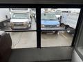 A blue 2021 Ford Econoline is parked among several other vehicles in a lot seen through a window