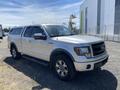 A 2014 Ford F-150 pickup truck in silver with a cab cover and black grill parked on gravel