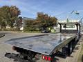 A 2022 Freightliner M2 106 flatbed truck with a shiny aluminum truck bed and rear lights visible