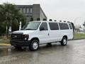 A white 2013 Ford E-350 van parked with multiple windows and a sliding side door