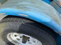 A close-up of a 2003 U-Built Reel Trailer's tire and fender showing wear and rust on the blue surface and a patterned tread on the tire