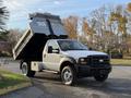 A white 2006 Ford F-550 dump truck with its bed raised is parked at an angle showcasing its truck bed and front profile