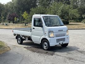 A white 2008 Suzuki Carry with a flatbed and a compact design parked on a paved surface