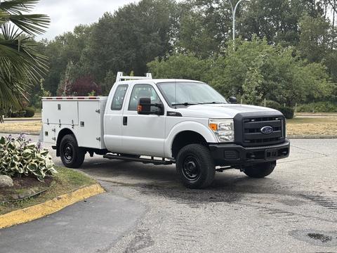 A white 2013 Ford F-250 SD pickup truck with a utility bed and black rims parked on a paved surface