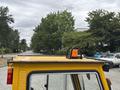 A yellow 2004 Bombardier SW48 with a light on the roof is parked on a street surrounded by trees and vehicles