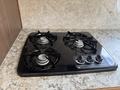 A black four-burner gas stove with silver knobs on a light-colored countertop