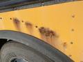 Close-up of a rusty section on a yellow 2006 Thomas Saf-T-Liner HDX bus showing several rust spots and corrosion along the metal surface