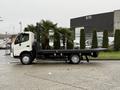 A 2015 Hino 195 flatbed truck with a white cab and black flatbed parked on a concrete surface with palm trees nearby