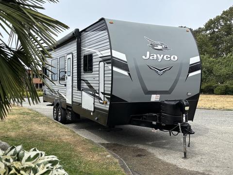 A 2021 Jayco Jay Flight travel trailer with a sleek gray exterior featuring the Jayco logo prominently displayed on the front and a hitch attached to the front tongue