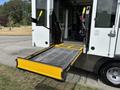 A wheelchair lift is extended from the back of a 2020 Chevrolet Express van with a metal mesh platform and safety rails