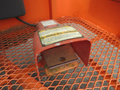 A red warning device with a yellow label resting on a metal platform the device has a protective cover and exposed coils