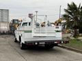 A white 2001 Ford F-350 work truck with a flatbed and utility body featuring a ladder rack and yellow and green stripes along the side
