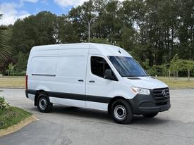A 2022 Mercedes-Benz Sprinter van in white with black trim and no windows on the cargo area is parked with its front facing slightly to the right