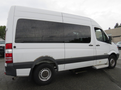 A white 2009 Dodge Sprinter Van with tinted windows and a gray stripe along the side parked to the side with visible wheels and step for entering