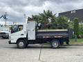 A 2015 Mitsubishi Fuso FE160 truck is parked on a concrete surface with a flatbed cargo area and a small storage unit attached to the side