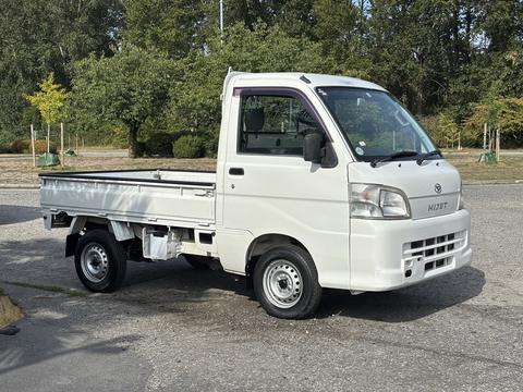 A 2010 Daihatsu Hijet compact pickup truck in white with a flatbed and a simple design featuring two doors and small wheels