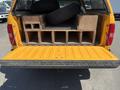 A 2013 Chevrolet Silverado 1500 with an open tailgate displaying wooden storage compartments and several stacked tires inside the bed