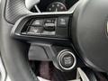 Close-up of a 2023 Alfa Romeo Giulia steering wheel featuring control buttons for cruise control and a round engine start stop button