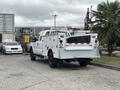 A white 2013 Ford F-250 SD utility truck with storage compartments in the bed and a ladder rack attached