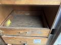 A wooden drawer with a worn interior and a brass handle partially opened inside a cabinet with another closed drawer below it