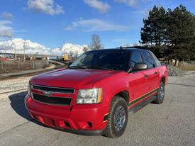 A red 2011 Chevrolet Avalanche with a black front grille and chrome accents parked at an angle with shiny wheels and a sleek body design