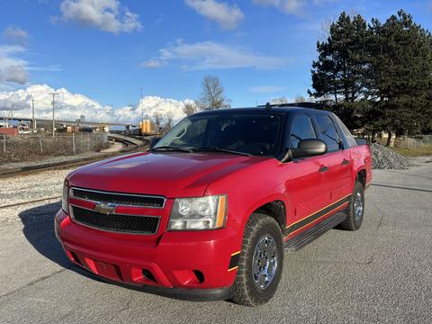 A red 2011 Chevrolet Avalanche with a black front grille and chrome accents parked at an angle with shiny wheels and a sleek body design
