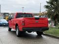 A red 2015 Ford F-150 parked on a wet surface showcasing its rear and side profile with a Ford logo on the tailgate and a black bed liner